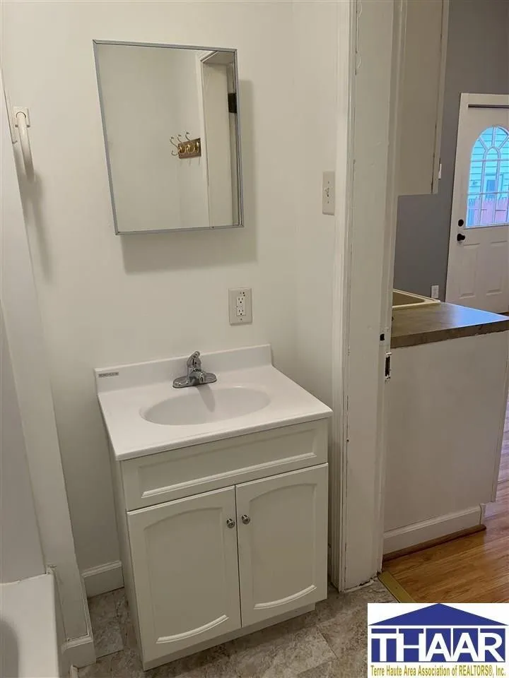 A bathroom with white walls and wooden floors.