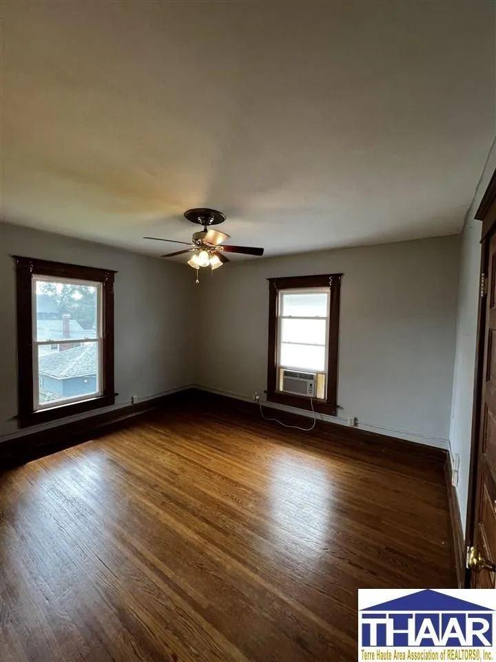 A room with wood floors and two windows.