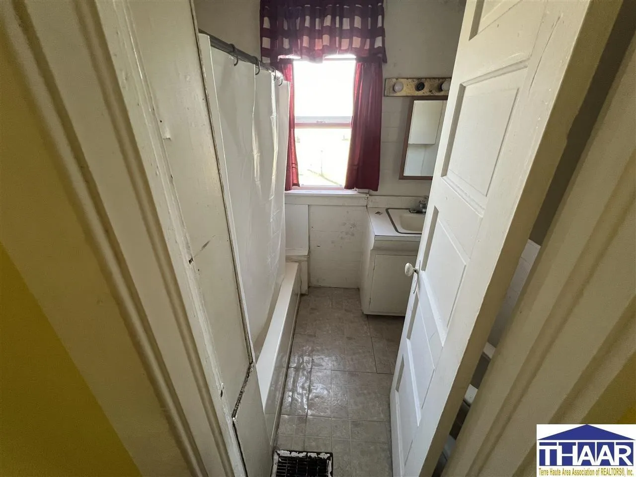 A small bathroom with a window and tiled floors.