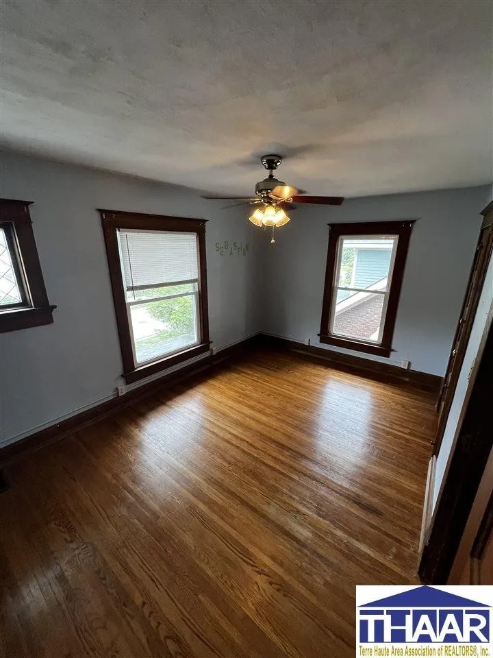 A room with two windows and a ceiling fan.