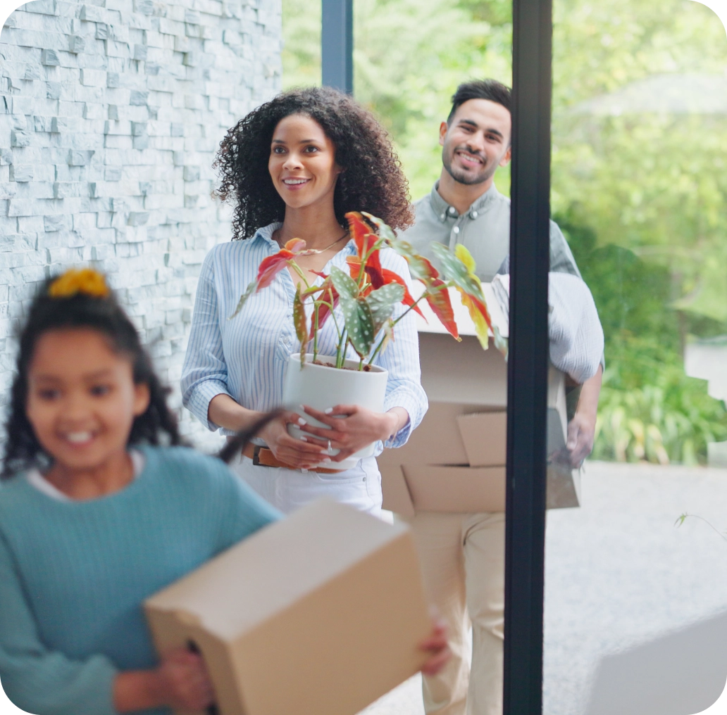 A family of three moves into their new home, cheerful and surrounded by boxes and a vibrant potted plant, marking the beginning of an exciting real estate adventure.